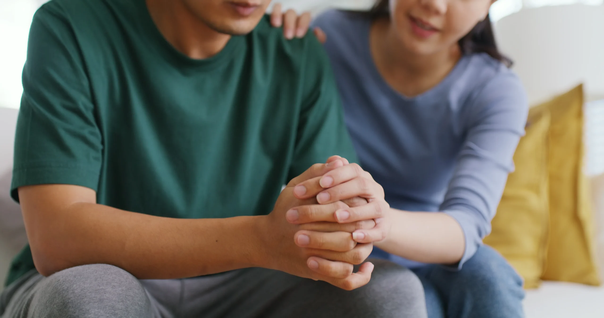 A man and woman sit together on a couch, holding hands, symbolizing connection and companionship.